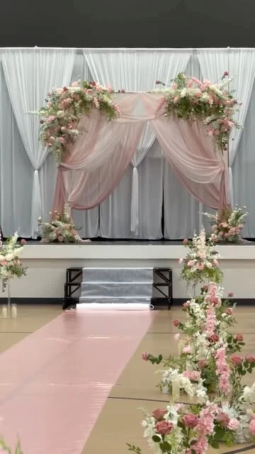 Wedding ceremony with blush drapes, florals, and a pink aisle